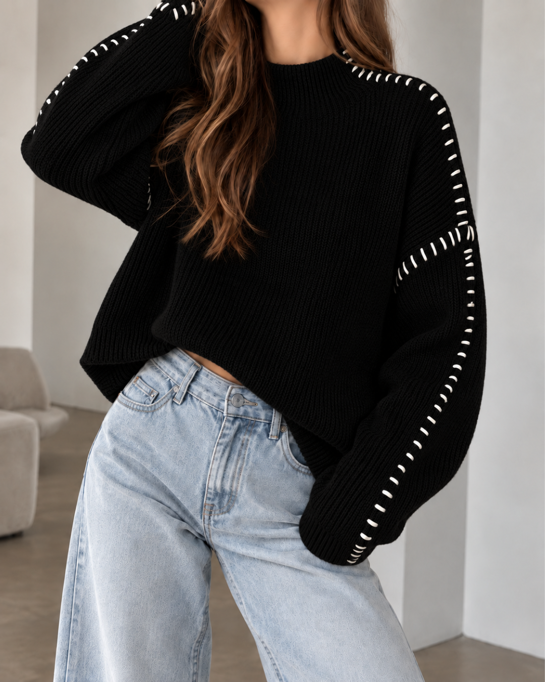 Pull oversize femme noir en maille côtelée, à col rond et manches longues amples, avec surpiqûres blanches contrastantes.