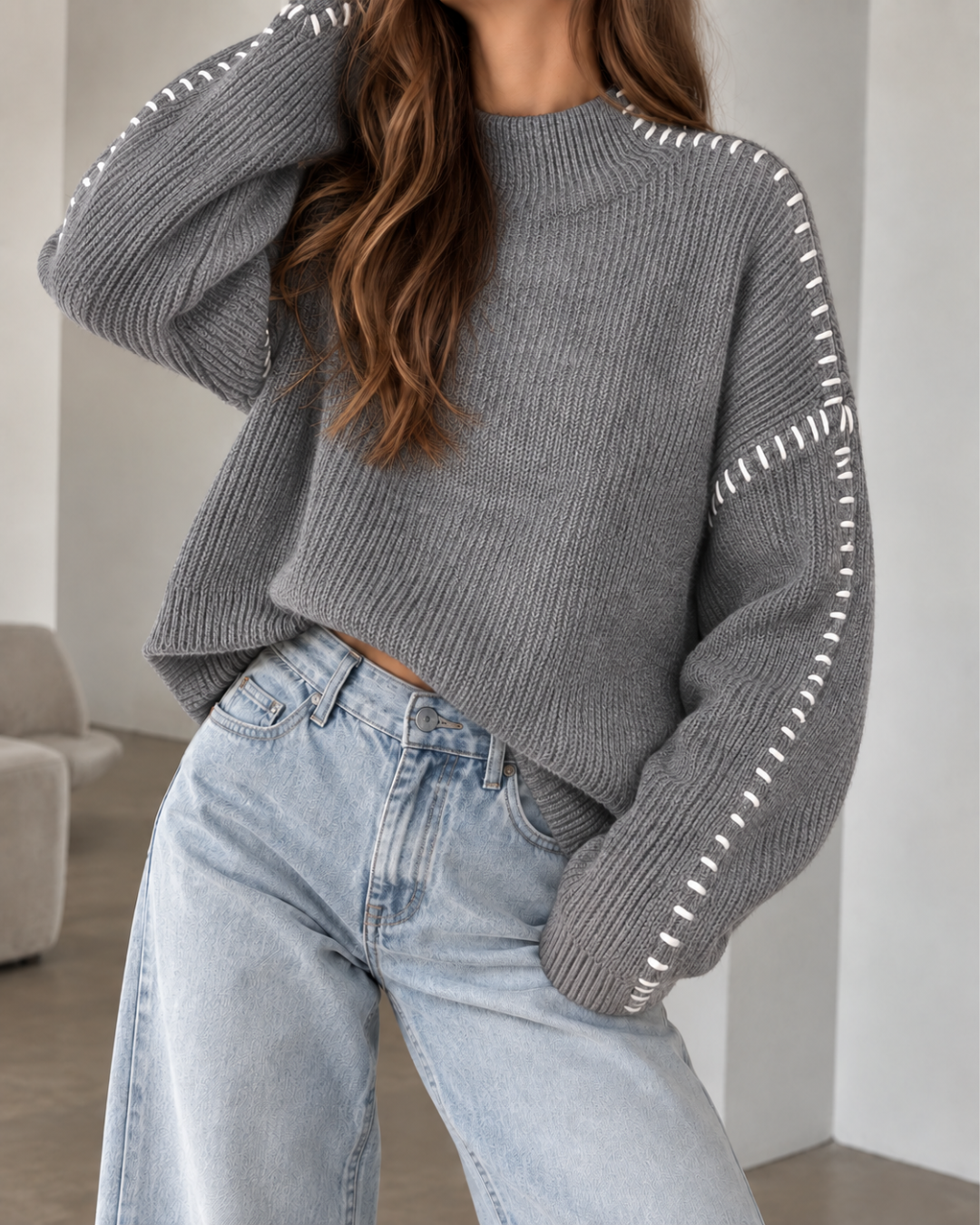 Pull oversize femme gris en maille côtelée, à col rond et manches longues amples, avec surpiqûres blanches contrastantes.