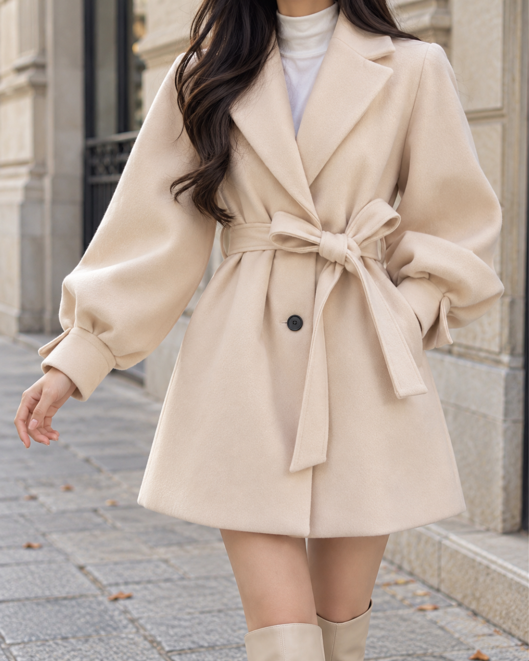 Manteau court évasé femme blanc cassé avec ceinture à nouer à la taille, col à revers, manches bouffantes volumineuses et fermeture boutonnée.