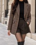 Blazer femme à carreaux marron et beige, coupe ajustée, col à revers, manches longues et poches à rabat, porté avec un short marron et un pull noir à col roulé.