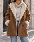 Manteau d’hiver femme marron en suédine, avec capuche, doublure en fausse fourrure écrue, manches longues et fermeture à brandebourgs.