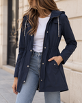 Veste mi-longue bleu marine pour femme avec capuche, taille ajustable, fermeture zippée et poches latérales.