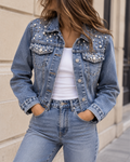Veste en jean bleu pour femme, coupe courte avec boutons métalliques, poches poitrine et détails ornés de perles et strass.