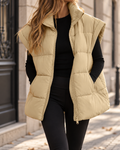 Gilet matelassé sans manches femme beige à col montant, fermeture zippée, poches latérales et coupe longue, porté avec un haut noir.