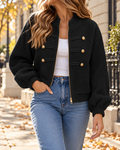 Veste courte femme noire en tissu texturé, avec fermeture zippée dorée, boutons décoratifs dorés, col rond et manches longues bouffantes, portée avec un jean bleu.