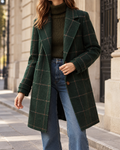 Manteau long femme vert foncé, avec col à revers, fermeture boutonnée, manches longues et poches latérales, porté avec un pull à col roulé et un jean bleu.